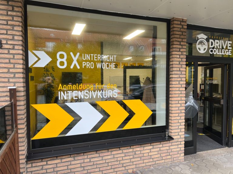 Schaufenster der Fahrschule Drive College mit gelben Chevron-Pfeilen und dem Hinweis „8× Unterricht pro Woche – Anmeldung für den Intensivkurs“